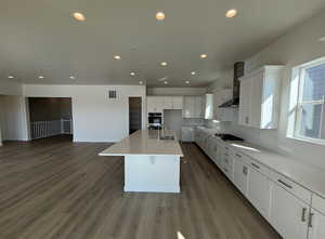 Kitchen featuring white cabinets, gas stovetop, dark wood-type flooring, a center island with sink, and wall chimney exhaust hood