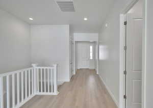 Hall with light wood finished floors, baseboards, visible vents, an upstairs landing, and recessed lighting