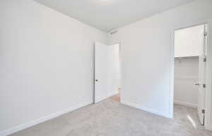 Unfurnished bedroom with a walk in closet, light carpet, and visible vents