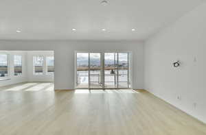 Unfurnished room featuring light wood finished floors, baseboards, a textured ceiling, a notable chandelier, and recessed lighting