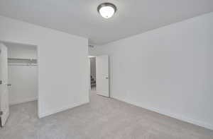 Unfurnished bedroom with baseboards, visible vents, light colored carpet, a textured ceiling, and a closet