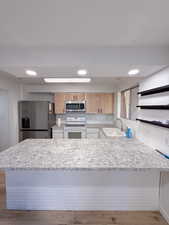 Kitchen with sink, stainless steel appliances, kitchen peninsula, and light stone countertops