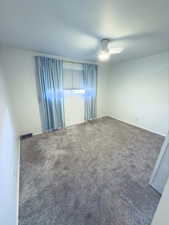 Empty room with ceiling fan and dark colored carpet