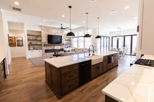 Kitchen featuring sink, light stone counters, dishwasher, pendant lighting, and a fireplace