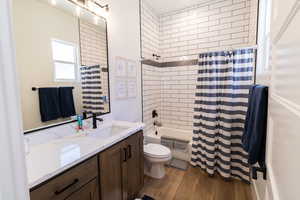 Full bathroom with hardwood / wood-style flooring, shower / tub combo with curtain, vanity, and toilet