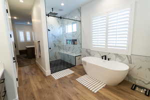 Primary Bathroom with wood-type flooring, separate shower and tub, plenty of natural light, and tile walls