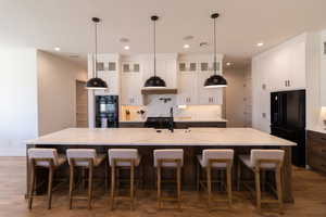 Kitchen with white cabinetry, light stone countertops, black appliances, and a spacious island