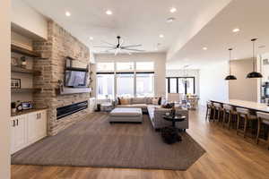 Living room with a large fireplace, ceiling fan, and light wood-type flooring