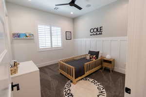 Carpeted bedroom with ceiling fan and a crib