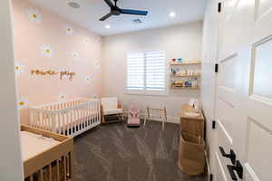 Carpeted bedroom featuring a crib and ceiling fan