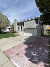 View of front facade with a chimney, concrete driveway, a front yard, and a garage