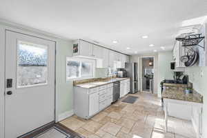 Kitchen with stainless steel appliances, white cabinetry, and light stone counters