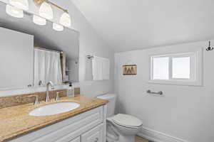 Bathroom featuring lofted ceiling, vanity, and toilet