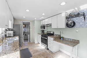 Kitchen with stainless steel appliances, white cabinetry, sink, and dark stone countertops