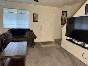 Living room featuring ceiling fan, light colored carpet, and a textured ceiling