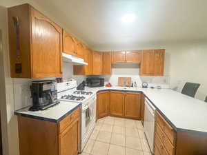 Kitchen with sink, white appliances, light tile patterned floors, and kitchen peninsula