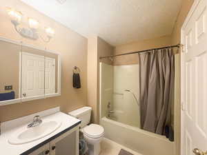 Full bathroom with shower / tub combo with curtain, tile patterned flooring, vanity, a textured ceiling, and toilet