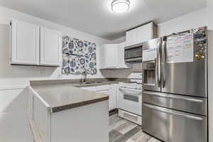 Kitchen with sink, light hardwood / wood-style flooring, appliances with stainless steel finishes, white cabinetry, and kitchen peninsula