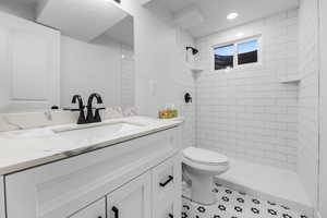 Bathroom with tile patterned flooring, vanity, tiled shower, and toilet