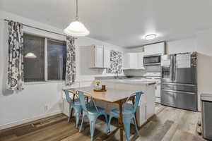 Kitchen with white cabinetry, stainless steel appliances, hanging light fixtures, and light hardwood / wood-style flooring