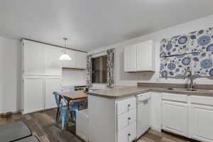 Kitchen featuring dark hardwood / wood-style floors, decorative light fixtures, white cabinetry, dishwasher, and sink