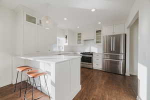 Kitchen with a breakfast bar, premium range hood, stainless steel appliances, white cabinets, and decorative light fixtures