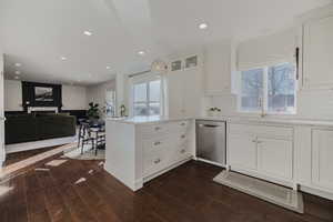 Kitchen with dark hardwood / wood-style floors, white cabinets, backsplash, stainless steel dishwasher, and kitchen peninsula