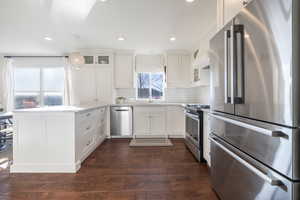 Kitchen with appliances with stainless steel finishes, white cabinets, dark hardwood / wood-style flooring, backsplash, and hanging light fixtures