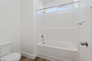 Clean white Bathroom with wood-style flooring, toilet, and shower/bathtub combination.