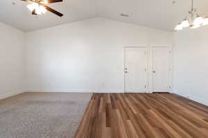 Unfurnished room with vaulted ceiling, ceiling fan with notable chandelier, and wood-style flooring.