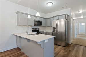 Kitchen featuring pendant lighting, stainless steel appliances, kitchen peninsula, and gray cabinetry.