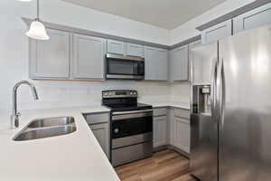 Kitchen featuring double sink, a textured ceiling, hanging pendant light fixtures, light wood-type flooring, and appliances with stainless steel finishes.