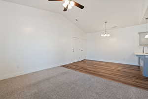 Unfurnished room with lofted ceiling, dark wood-type flooring, and ceiling fan as well as a beautiful chandelier in dining area.