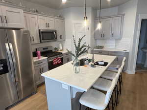 Kitchen featuring appliances with stainless steel finishes, gray cabinetry, hanging light fixtures, a kitchen breakfast bar, and a center island with sink