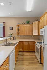 Kitchen with light brown cabinetry, tasteful backsplash, sink, light wood-type flooring, and white appliances