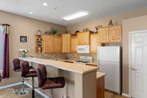 Kitchen featuring a breakfast bar, light wood-type flooring, light brown cabinets, kitchen peninsula, and white appliances