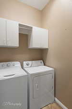 Clothes washing area with cabinets, separate washer and dryer, light hardwood / wood-style flooring, and a textured ceiling