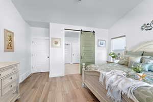 Bedroom with a barn door, vaulted ceiling, and light wood-type flooring