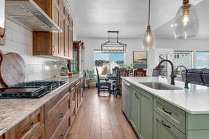 Kitchen featuring sink, green cabinets, stainless steel appliances, wall chimney range hood, and light hardwood / wood-style flooring