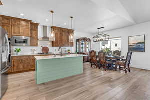 Kitchen featuring sink, tasteful backsplash, decorative light fixtures, appliances with stainless steel finishes, and wall chimney range hood