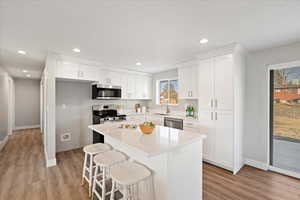 Kitchen featuring appliances with stainless steel finishes, a breakfast bar, sink, white cabinets, and a center island