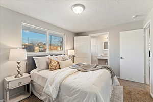 Bedroom featuring ensuite bath, carpet, and a textured ceiling