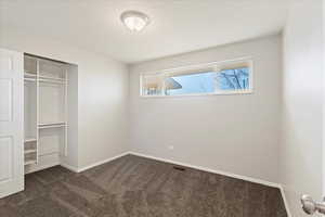 Unfurnished bedroom with a closet, a textured ceiling, and dark colored carpet