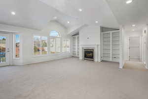 Unfurnished living room featuring light colored carpet, vaulted ceiling, built in features, and a textured ceiling