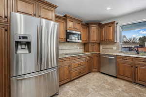 Kitchen featuring sink, backsplash, light stone countertops, and appliances with stainless steel finishes