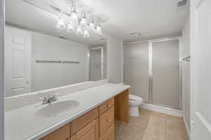 Bathroom featuring vanity, a textured ceiling, tile patterned floors, toilet, and walk in shower