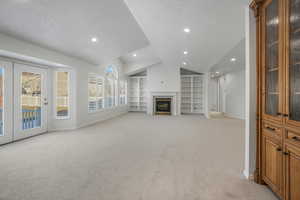 Carpeted living room with lofted ceiling, built in shelves, and a textured ceiling