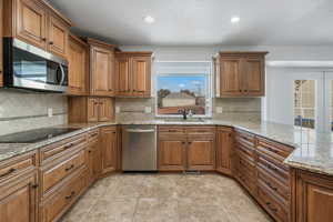 Kitchen with appliances with stainless steel finishes, tasteful backsplash, sink, light tile patterned floors, and light stone counters