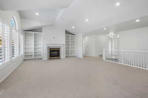 Unfurnished living room featuring lofted ceiling, light colored carpet, built in features, and a fireplace