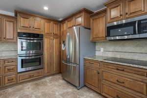 Kitchen with appliances with stainless steel finishes, light stone counters, and decorative backsplash